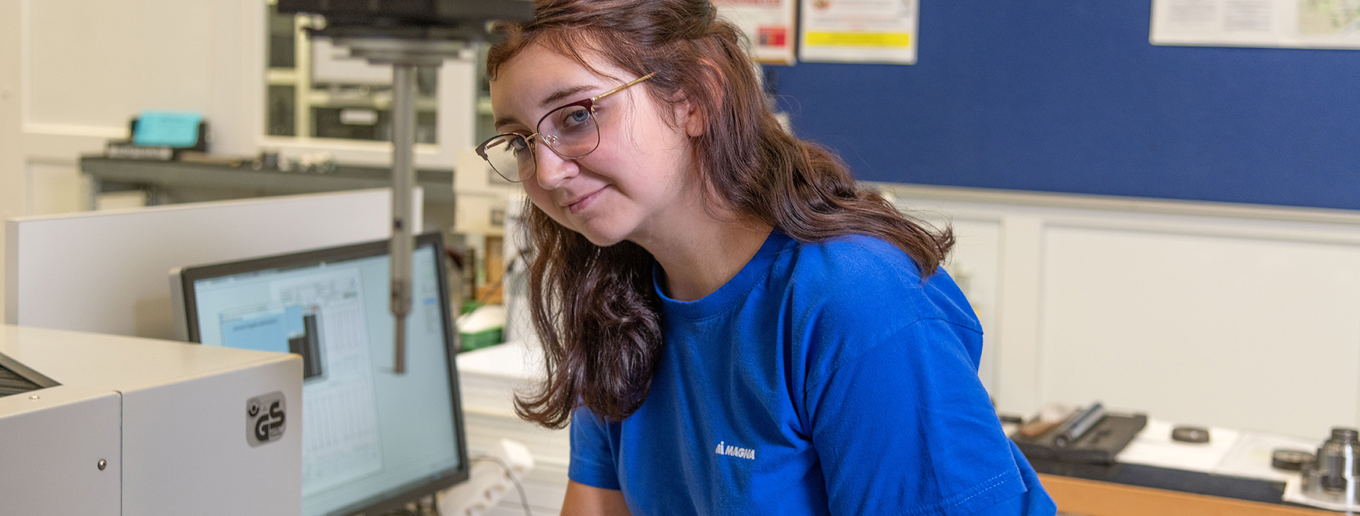 Worker in a blue shirt using testing equipment to analyze a component in a lab setting