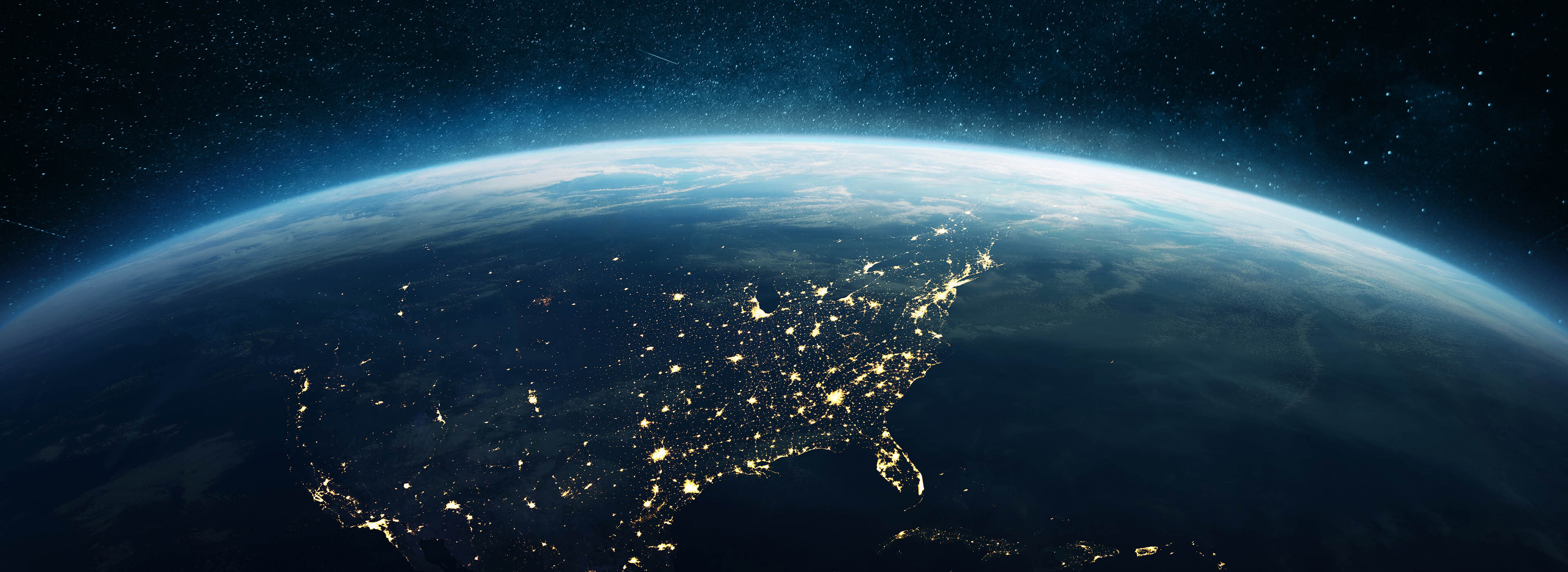 View of Earth from space, showing illuminated city lights across North America against a dark, starry sky.