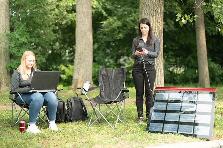 Two people charging thermoplastic roof panel with smart phone