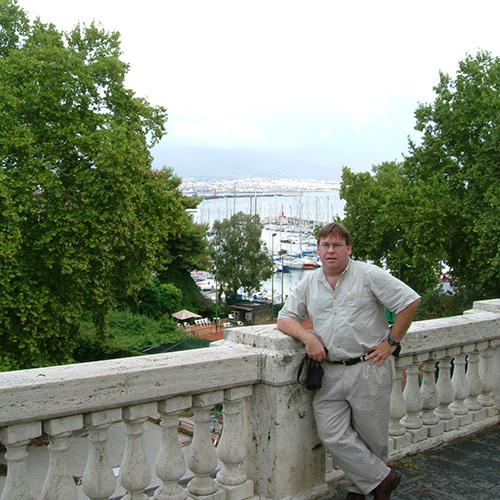 Doug Plester standing on a bridge with a marina in the background in Italy