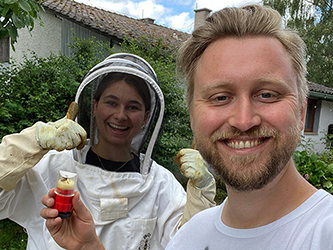 Alessandro Heuberger with his grandfather standing beside their bee hives in a field