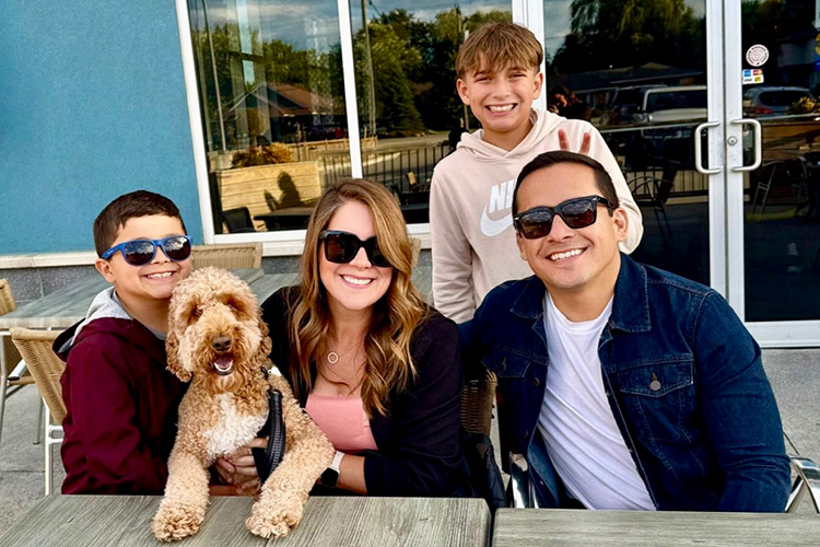 Two adults, two children and a dog sitting at a table outside in the summer