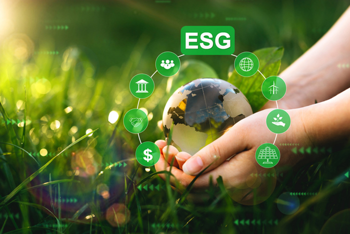 Hands holding a globe surrounded by ESG icons on a grassy background